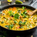 A large black cast iron skillet filled with Yellow Thai Curry with lime wedges and cilantro sprigs around it.