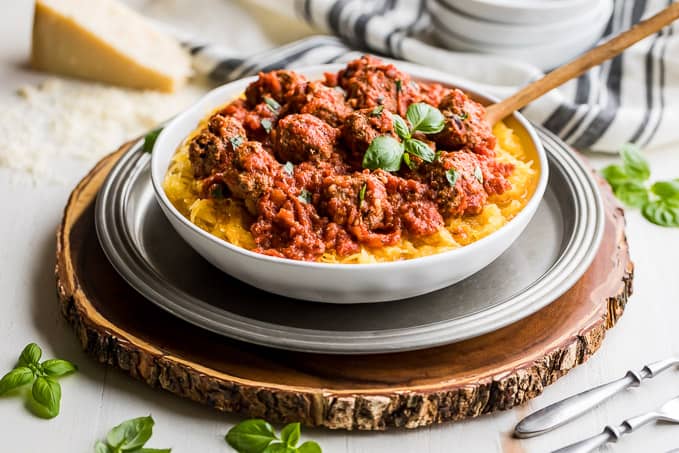 A large white bowl filled with cooked spaghetti squash and topped with tomato meatballs sauce.