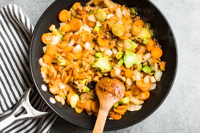 Adding the curry paste to the sautéed veggies in a large skillet.