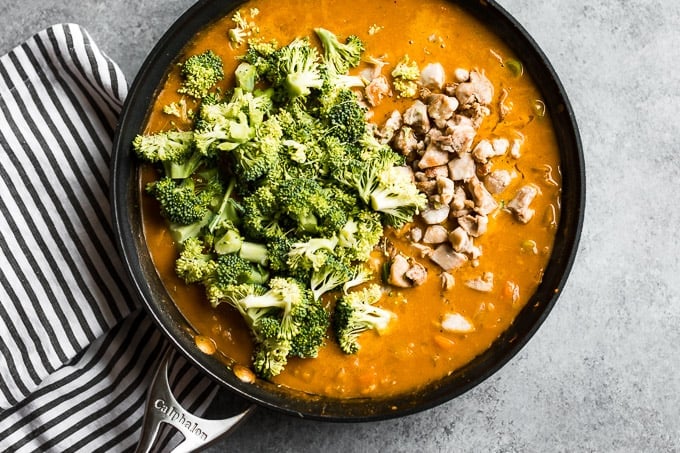 Adding the cooked chicken and broccoli florets to the curry in a large skillet.