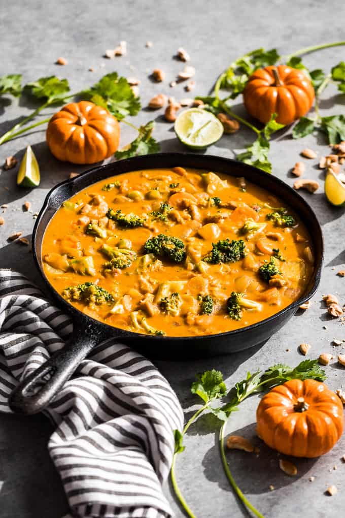 Side view of Pumpkin Curry in a cast iron skillet with mini pumpkins, cashews and cilantro around it.