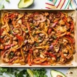 A large cookie sheet with Chicken Fajitas with lime wedges, salsa, and tortillas around it.