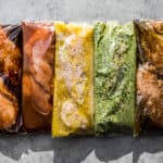5 healthy Instant Pot Chicken Marinades in plastic Ziplock bags laid in a row on a grey background.