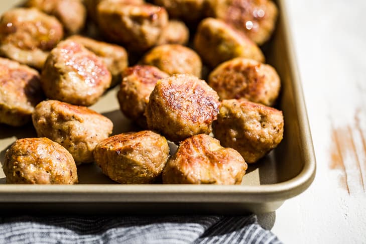 Baked turkey meatballs on a gold baking sheet with a blue linen next to it.