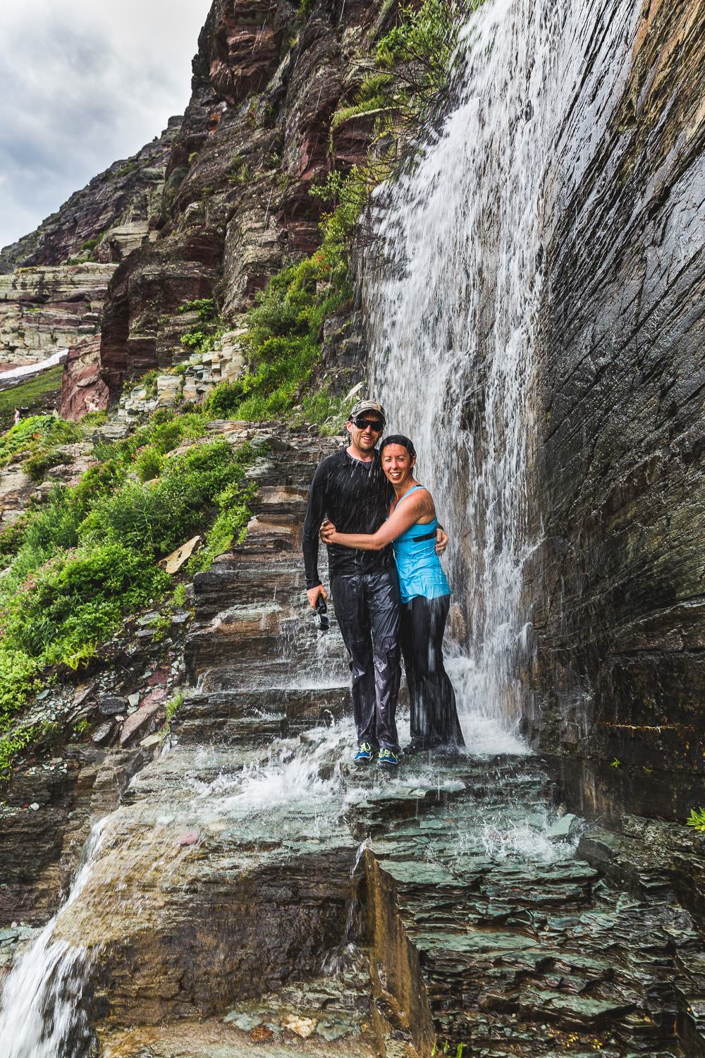Tyler & Kari standing in a waterfall in Glacier National Park