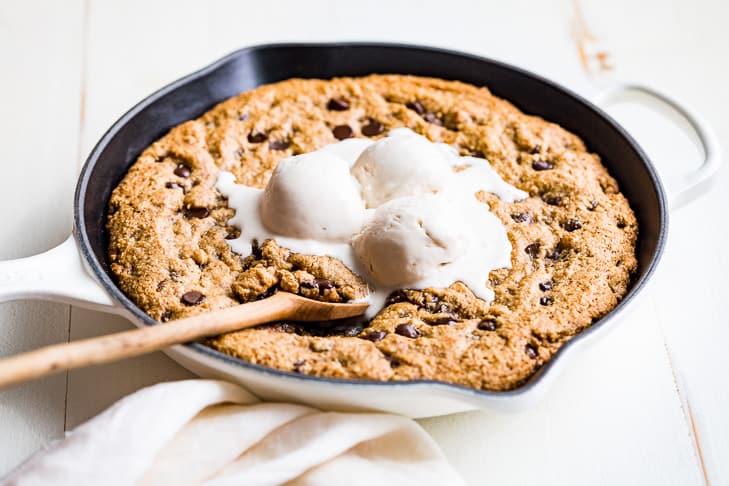 Chocolate Chip Skillet Cookie with ice cream on top and a wooden spoon scooping some out.