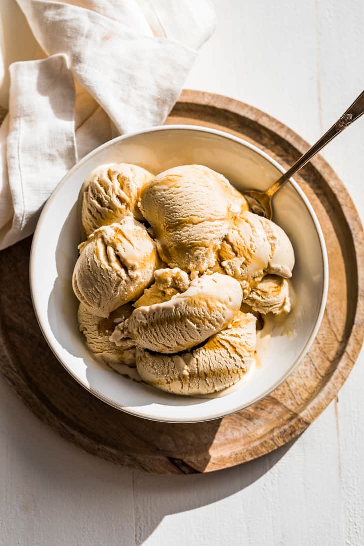 Scoops of maple ice cream in a white bowl set on a round wood cutting board.