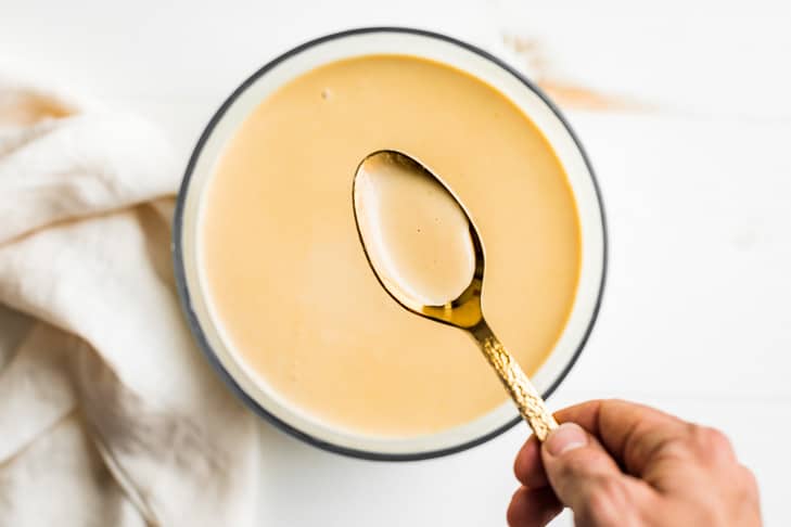 A hand holding a gold spoonful of custard up close to show the texture of the finished custard.