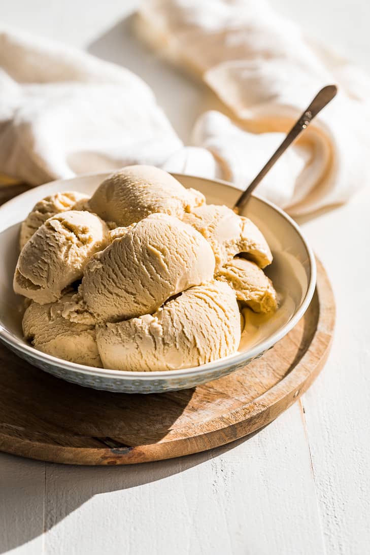 Scoops of fully frozen maple ice cream in a bowl with blue on the outside set on a round wood cutting board.