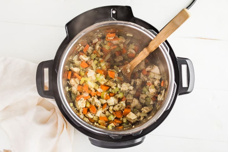 Adding the chicken to the veggie mixture in the Instant Pot as the second step.