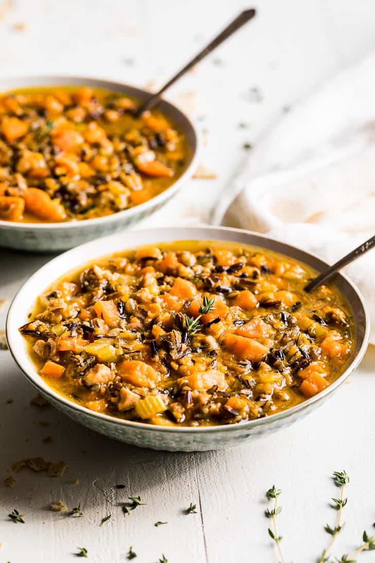 Two bowls of chicken and wild rice soup with sweet potatoes on a white background.