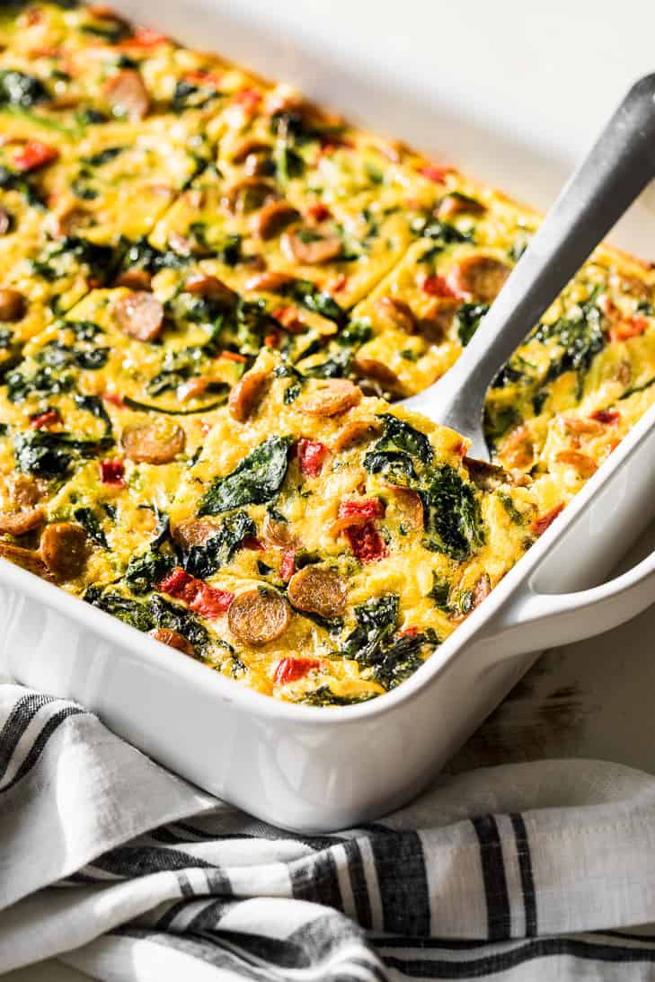 Loaded overnight breakfast casserole in a white baking dish cut into slices.