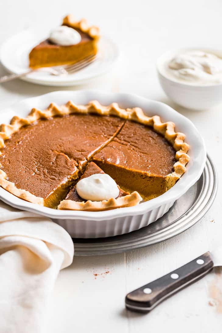 A side view of the paleo pumpkin pie with whipped cream and a slice on a white plate.