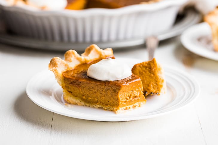 A slice of paleo pumpkin pie with whipped cream and a bite on the fork.
