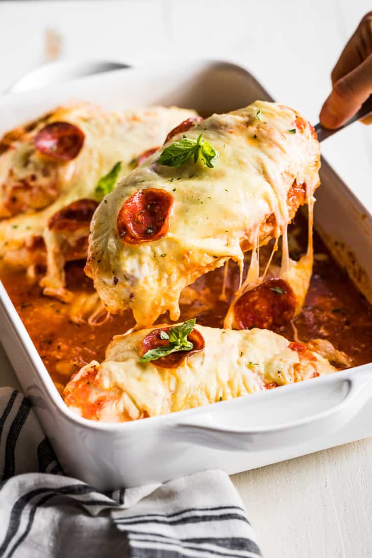 Easy Pizza Stuffed Chicken in a white baking dish being lifted out with a spatula.