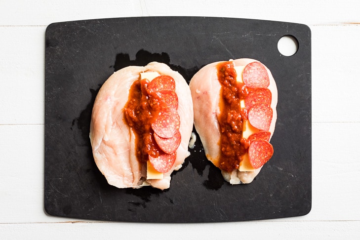 The process of cutting open the chicken breasts, with the pizza ingredients laid on top.