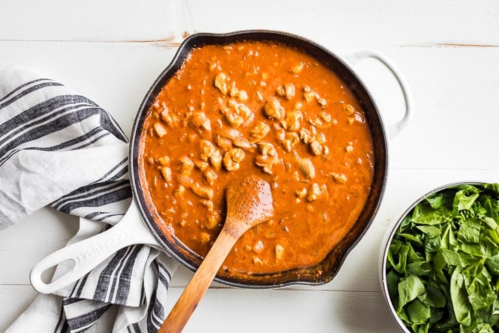 The berbere curry sauce simmered down in a white skillet and the chicken being added back in.