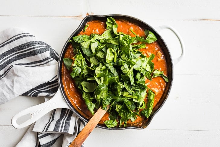 The final recipe step of adding the spinach to the curry to wilt it.