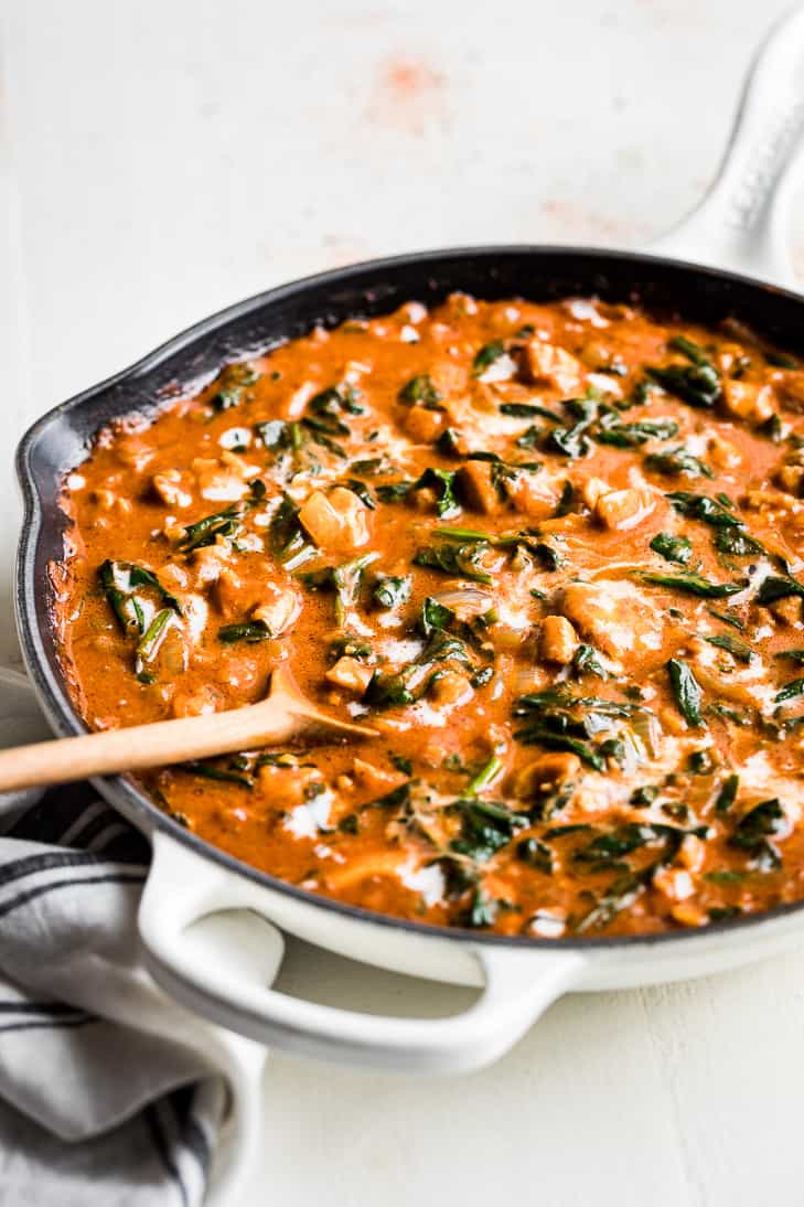 Ethiopian Berbere Chicken Curry in a white skillet on a white background with a wooden spoon.