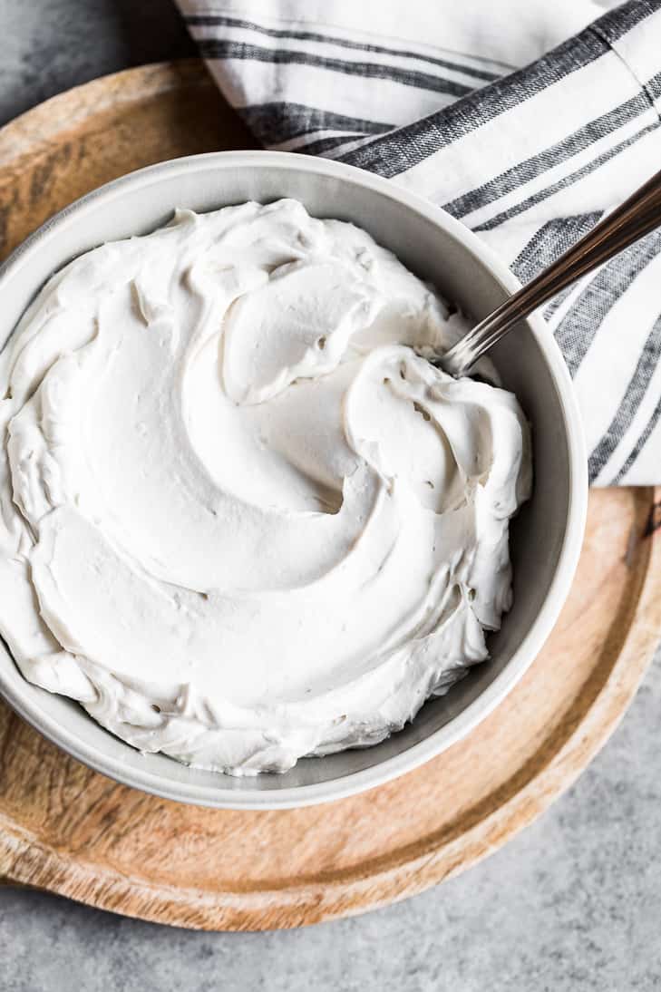 Giant grey bowl of dairy free coconut whipped cream placed on a round wooden board with a striped linen.