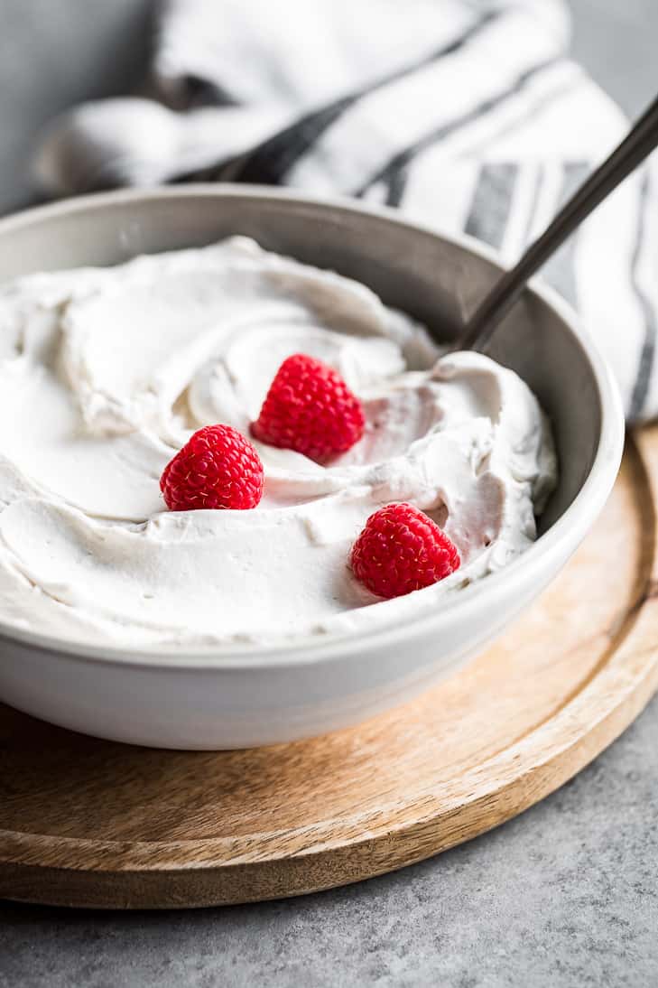 Grey bowl filled with coconut whipped cream and topped with three raspberries.
