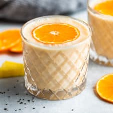 Two glasses of smoothie with orange slices around and a blue linen.