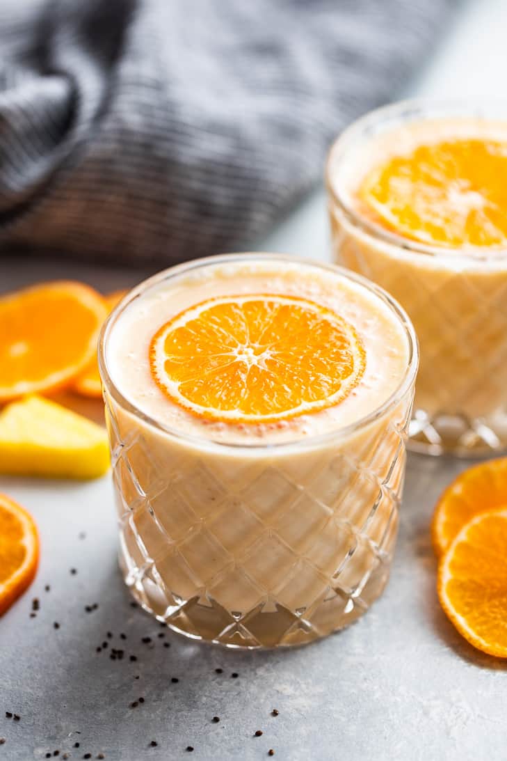 Two glasses of Pineapple Orange Banana Smoothie with orange slices on top and around the glasses.