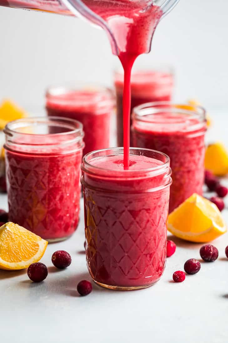 Cranberry orange smoothie being poured from the blender into glasses.