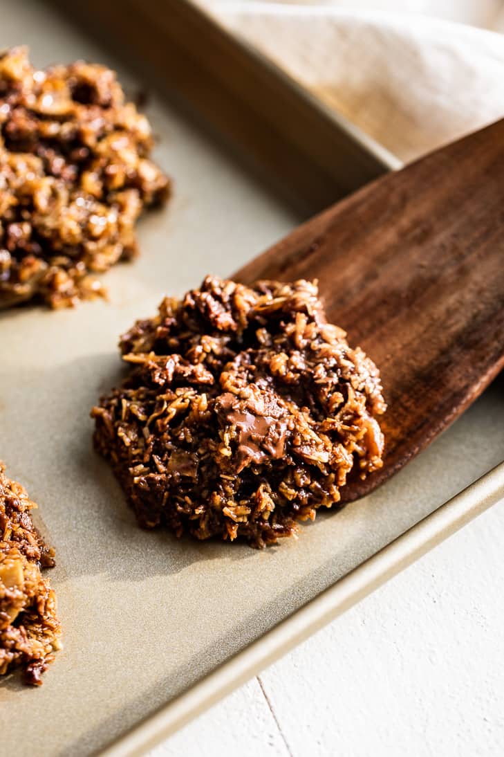 Wooden spatula scooping up a Chocolate Chip Salted Caramel Cookie from a gold cookie sheet.