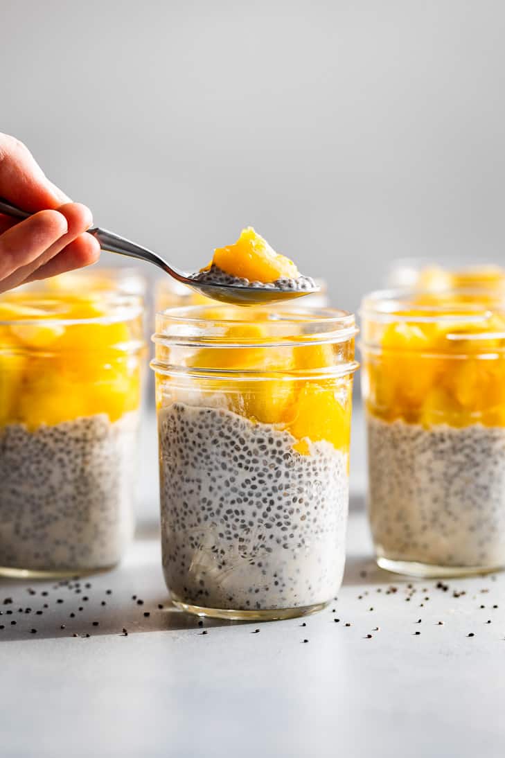 A spoonful of Cream Coconut Pudding with a mango chunk being lifted out of the mason jar.