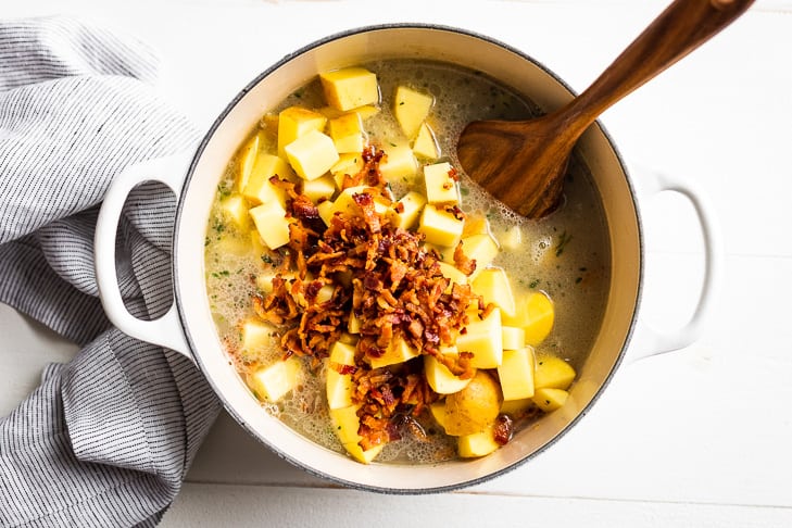 The next step of adding the potatoes, bacon, and liquids to the soup pot before simmering the clam chowder.