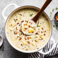 A large soup pot full of Creamy Dairy Free Clam Chowder with a small bowl of bacon bits, ground pepper and striped linen.