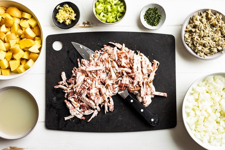 All of the ingredients prepped for the Creamy Dairy Free Clam Chowder and placed into prep bowls with chopped bacon on the cutting board.