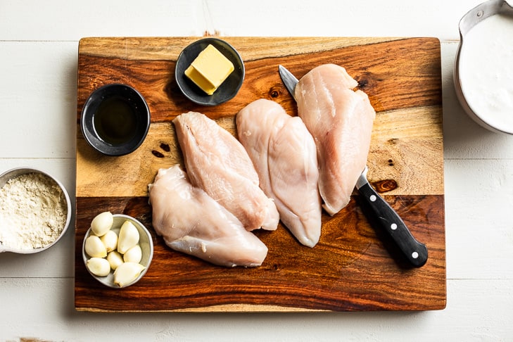 All the ingredients for the Creamy Garlic Chicken prepped on a wooden cutting board.