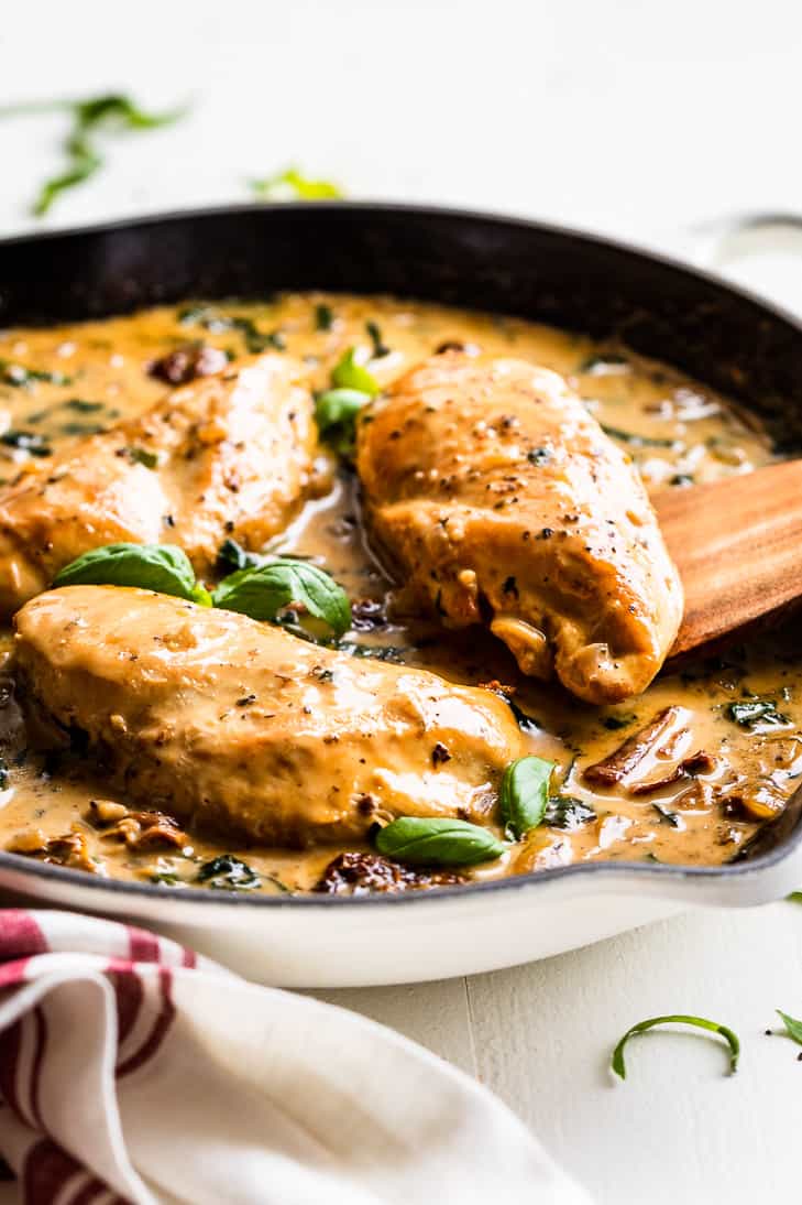 Creamy Tuscan Chicken in a white skillet with basil leaves on top.