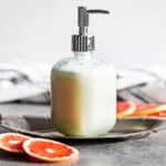 Pump bottle filled with Grapefruit Body Wash on a silver tray with grapefruit slices around it.