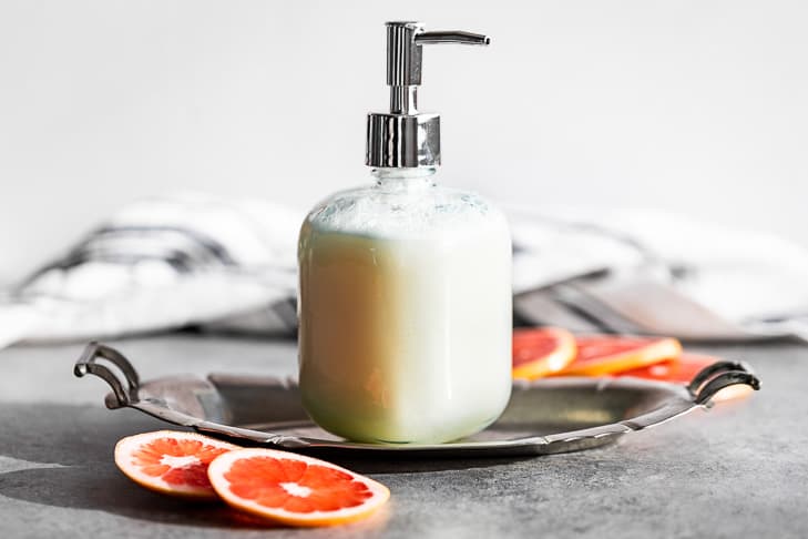 Pump bottle filled with Grapefruit Body Wash on a silver tray with grapefruit slices around it.