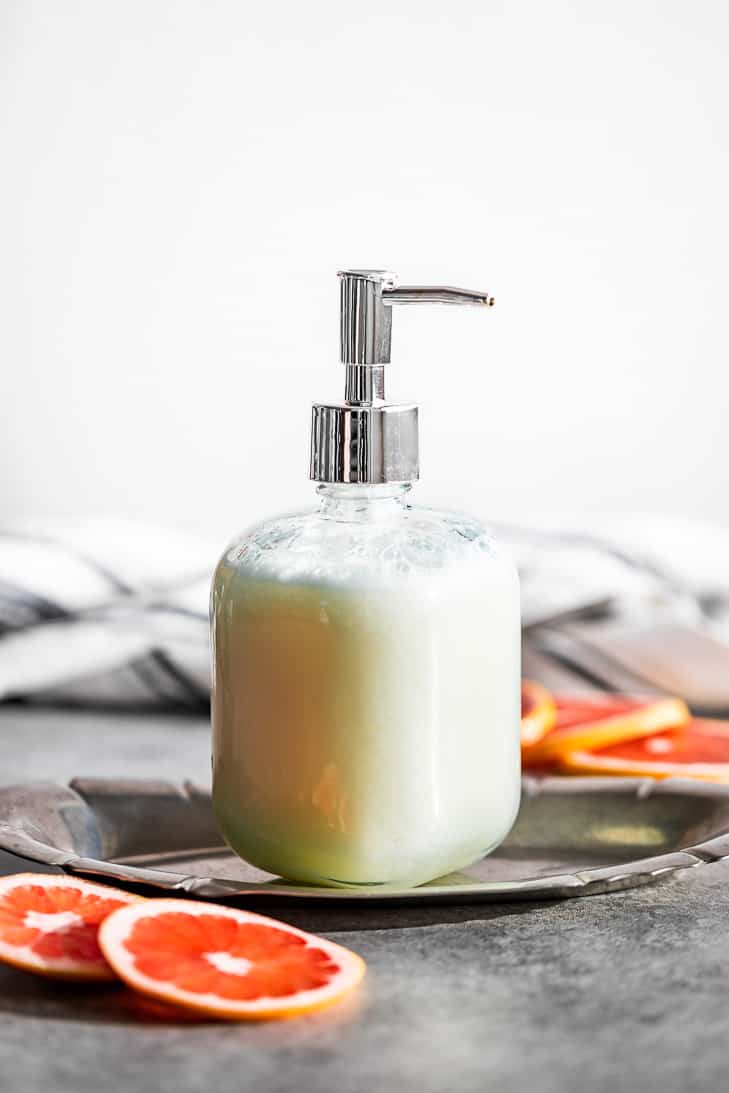 A soap pump bottle full of Grapefruit Ginger Body Wash set on a silver plate with grapefruit slices placed around it.