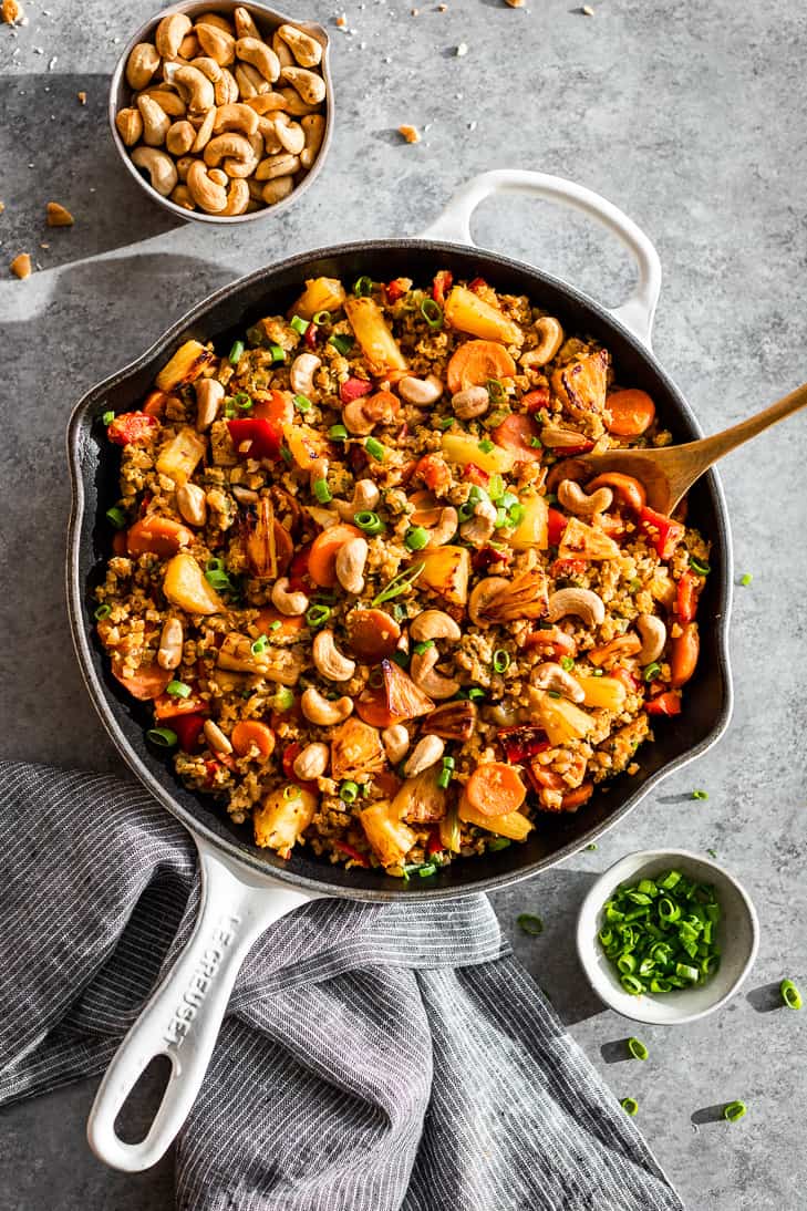 Pineapple Cauliflower Fried Rice in a large white skillet with a bowl of toasted cashews and a bowl of sliced green onions on the side.