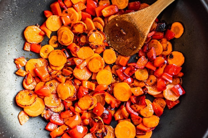 The second step in the recipe sautéing the carrots and bell pepper together in a skillet.