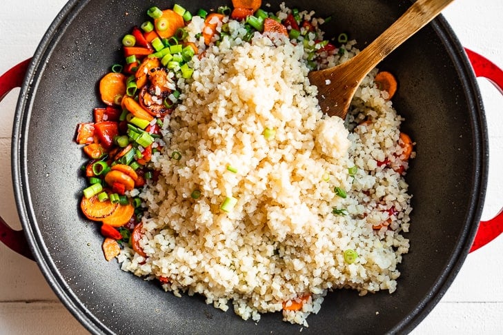 Adding the cauliflower rice to the pan with the stir fried veggies.