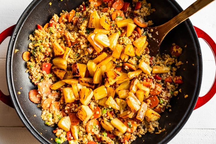 Adding the stir fried pineapple to the finished cauliflower rice as the final step.