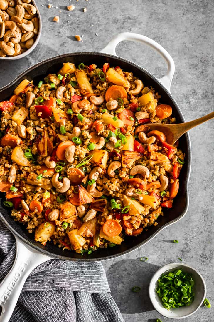 Paleo Pineapple Cauliflower Fried Rice in a white skillet with a wooden spoon.