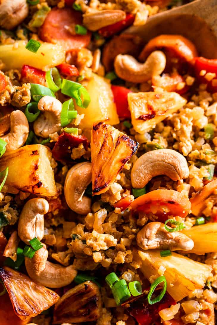 A close up photo of Paleo Pineapple Cauliflower Fried Rice being spooned out with a wooden spoon.