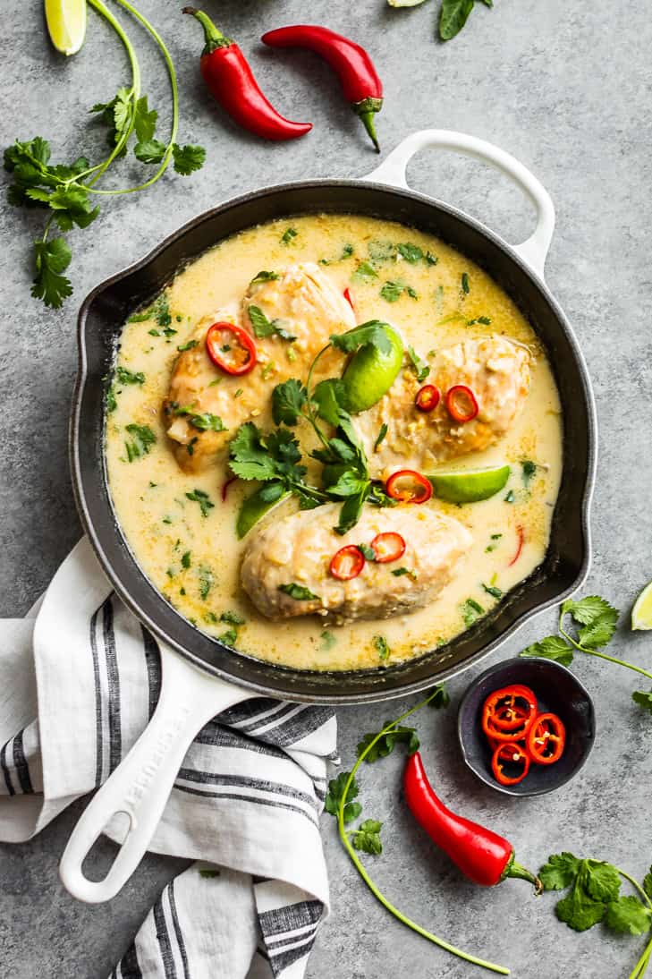 Thai Coconut Lime Chicken in a white skillet with chilis, cilantro, and lime wedges around it.