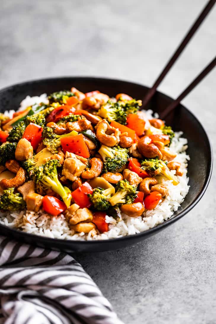 Cashew Chicken over steamed rice in a black bowl with chopsticks.