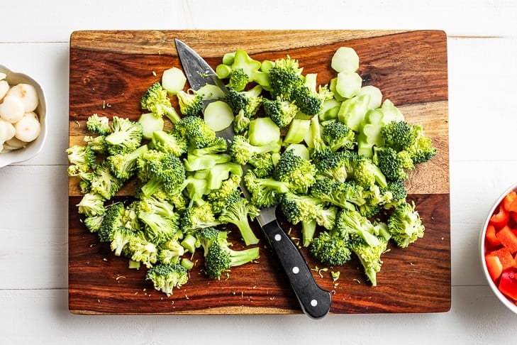 Chopping up the broccoli on a wooden cutting board.