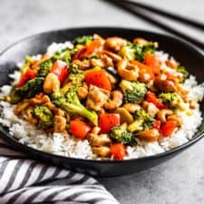 A black bowl with steamed rice topped with cashew chicken.