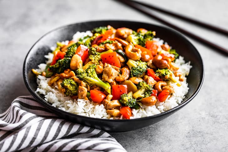 A black bowl with steamed rice topped with cashew chicken.