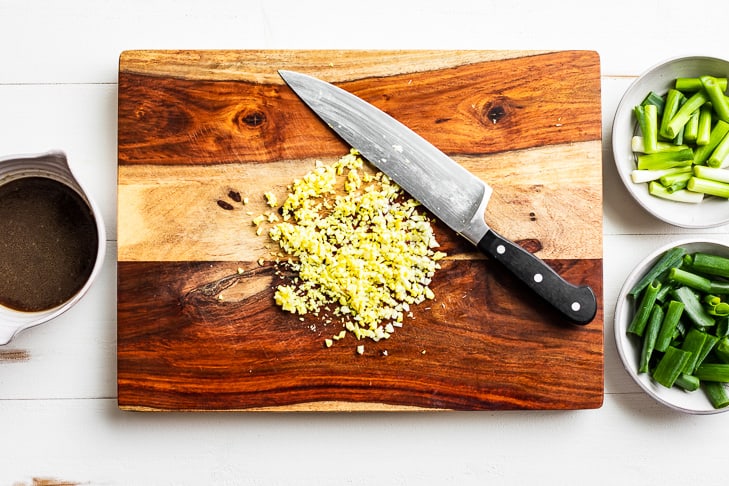Mincing the garlic and ginger on a wooden cutting board.